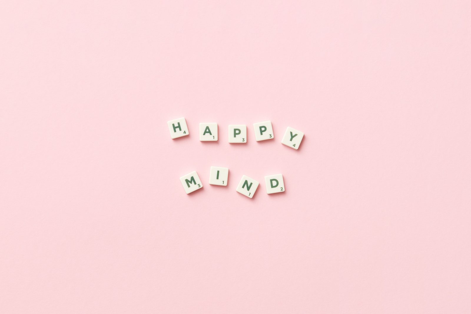 Scrabble tiles spelling 'Happy Mind' on a pink background